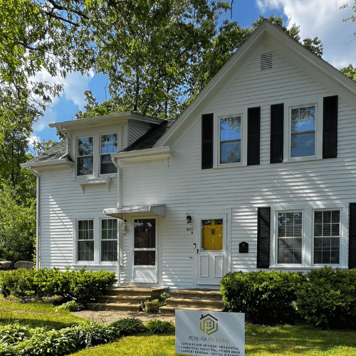 Painter on a ladder working on a two-story house exterior.